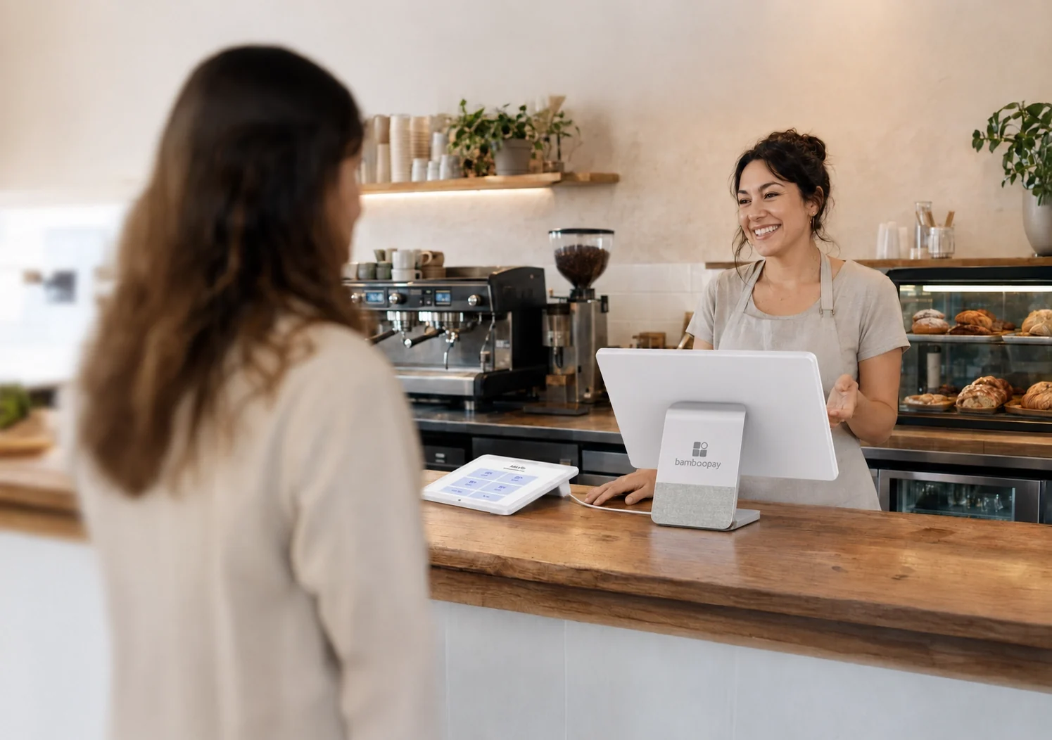 Barista behind a cafe counter, a Go POS screen turned toward the customer