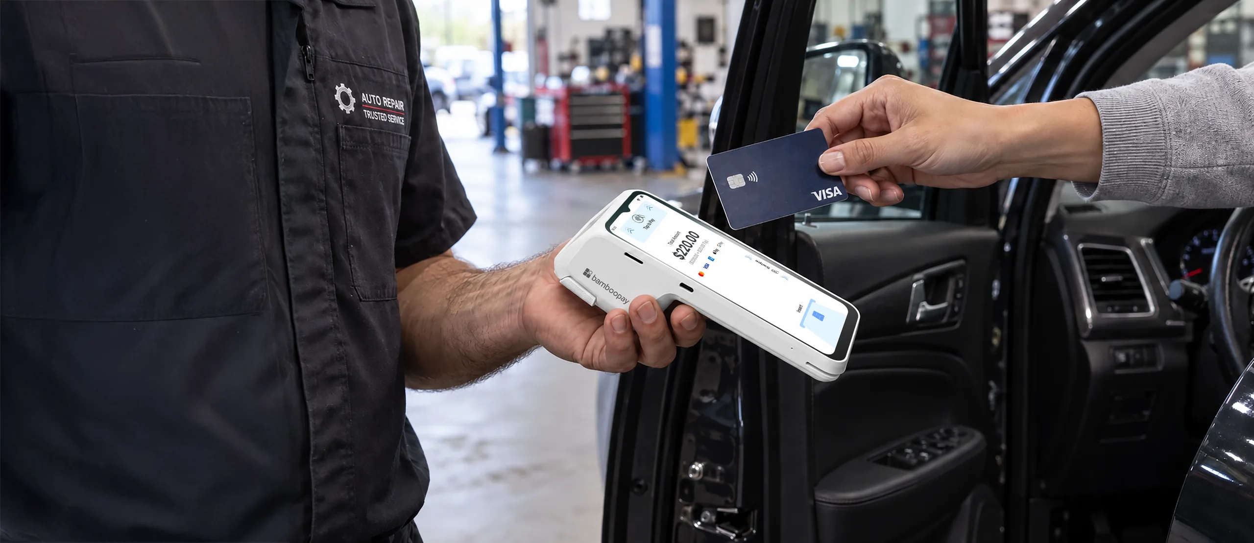 Auto technician taking a tap payment on a Go POS handheld beside a customer's car